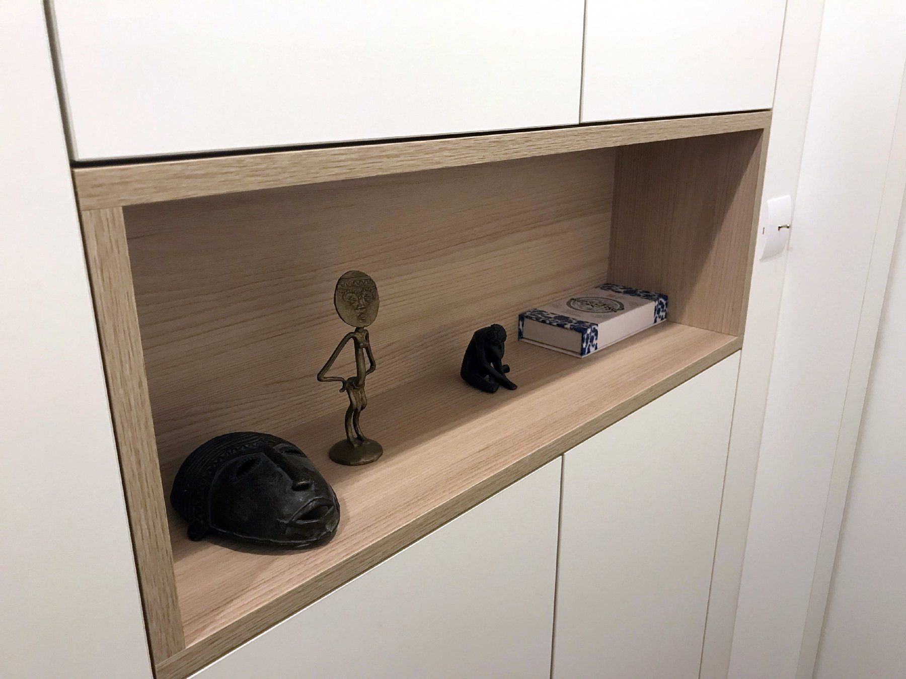 Étagère murale intégrée avec portes d'armoire blanches et petits objets décoratifs sur une tablette en bois