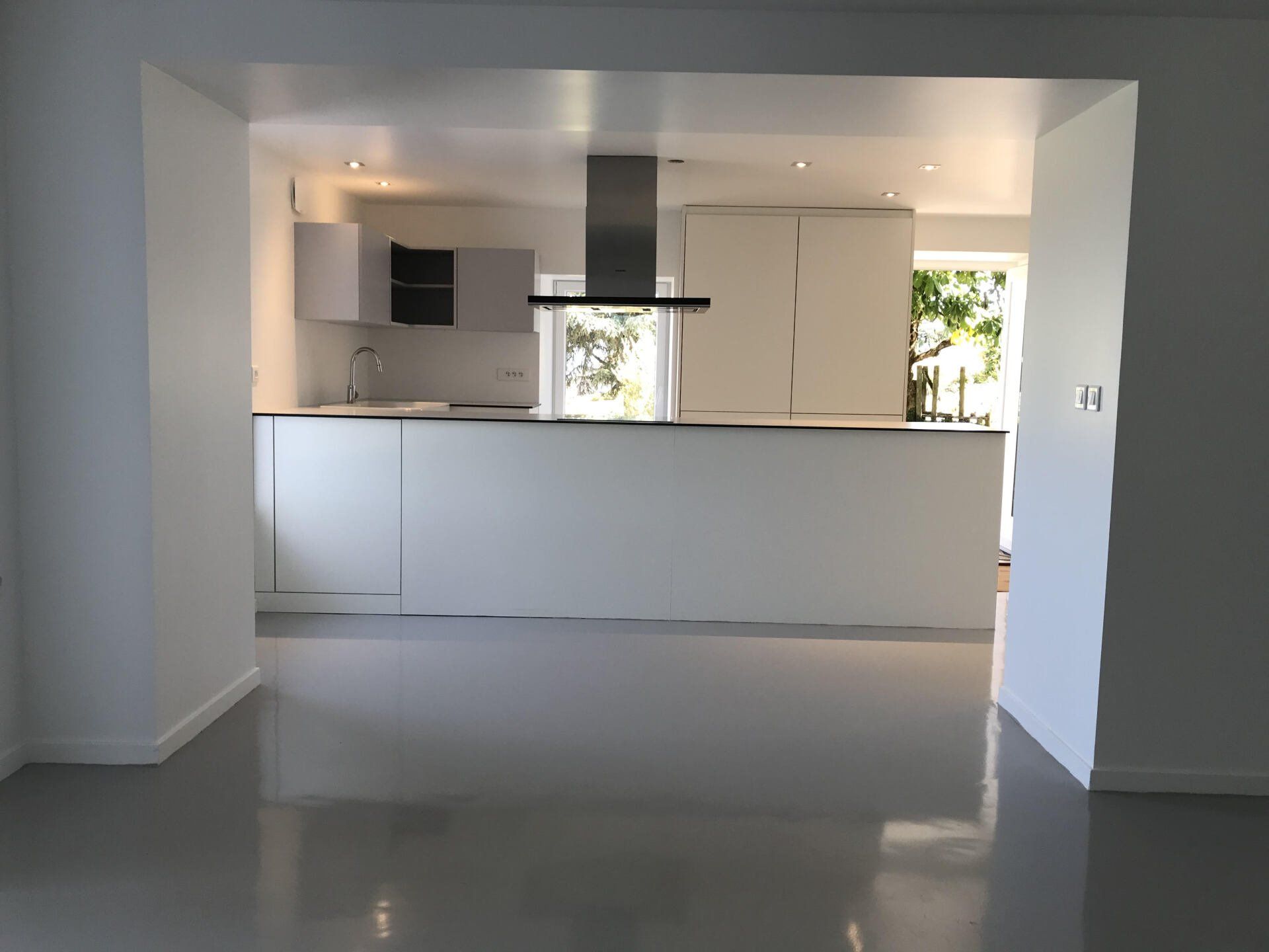 Cuisine moderne lumineuse et vide, avec des armoires blanches et un grand îlot visible à travers une large porte.