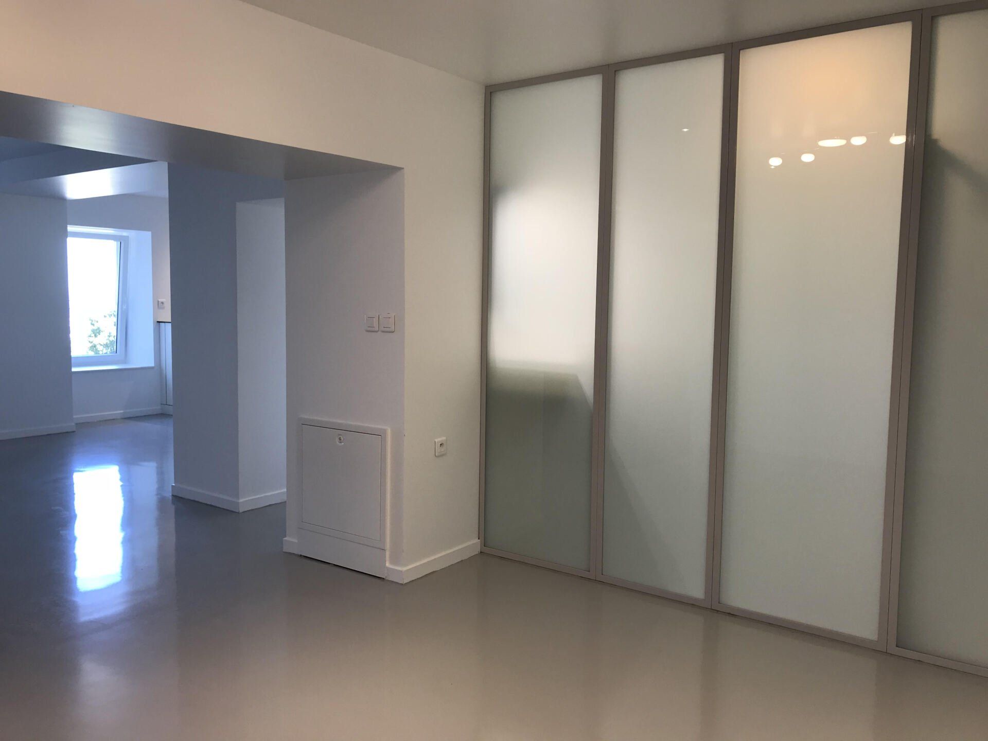 Pièce moderne vide avec sol gris brillant, portes coulissantes en verre dépoli et une porte ouverte sur un espace lumineux