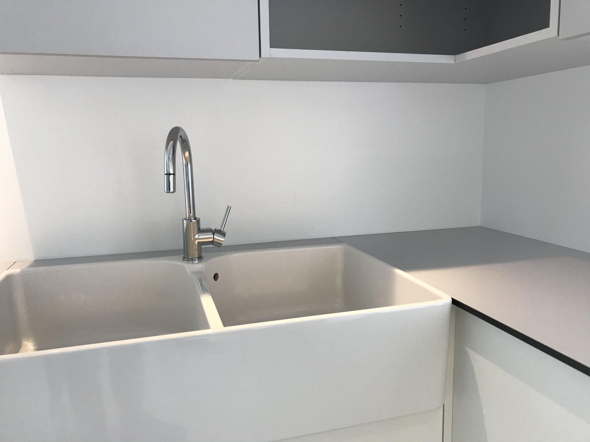 Évier de cuisine moderne à double cuve blanche, robinet chromé et plan de travail gris sur un mur clair