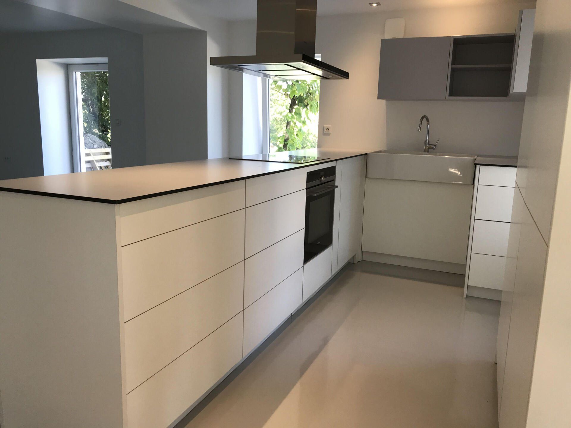 Cuisine moderne blanche avec îlot central, hotte aspirante en inox et évier près d'une fenêtre lumineuse