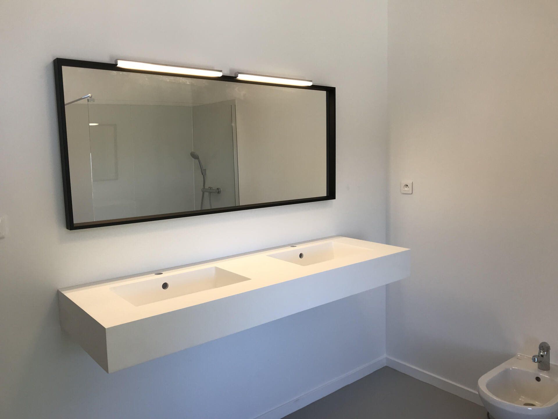 Salle de bains moderne avec double vasque suspendue, grand miroir et murs blancs.