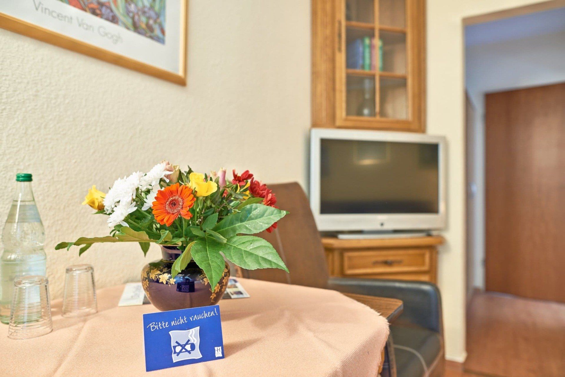 Auf einem Tisch vor einem Fernseher steht eine Vase mit Blumen.