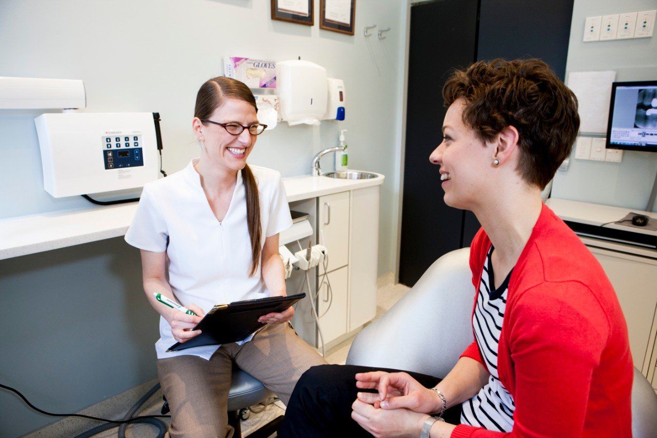 A woman is sitting in a dental chair talking to a female hygienist.