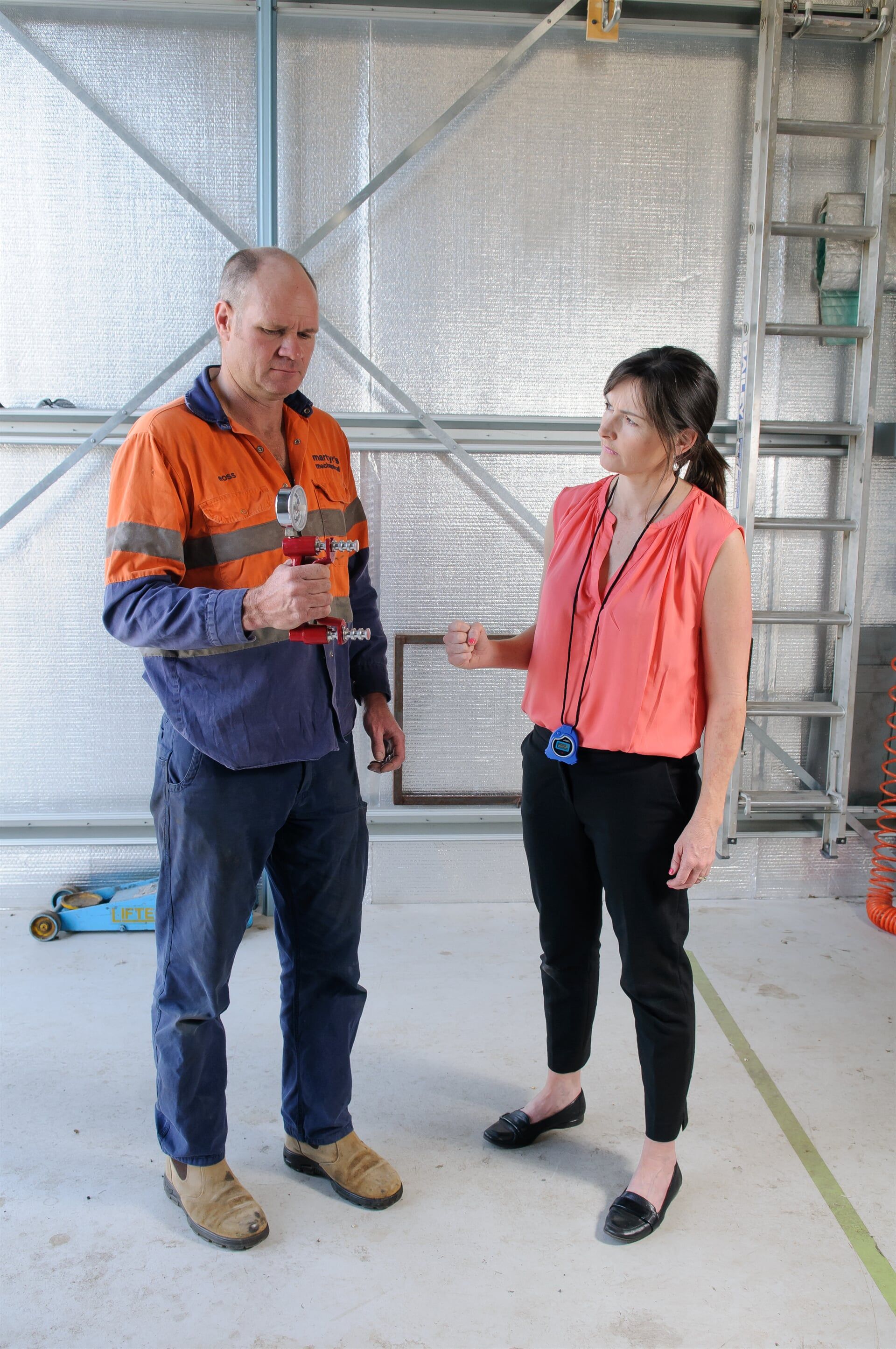 Two people talking in a construction site, one in an orange safety jacket and the other in a pink vest. — Health Experts In Toowoomba, QLD