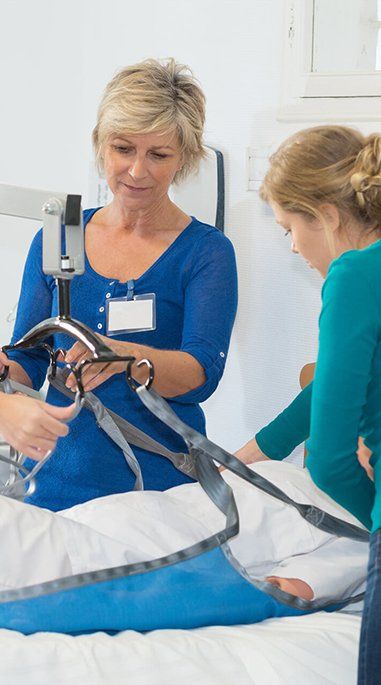 Caregiver and nurse lift a patient on a sheet in a hospital room using a blue hoist. — Health Experts In Toowoomba, QLD