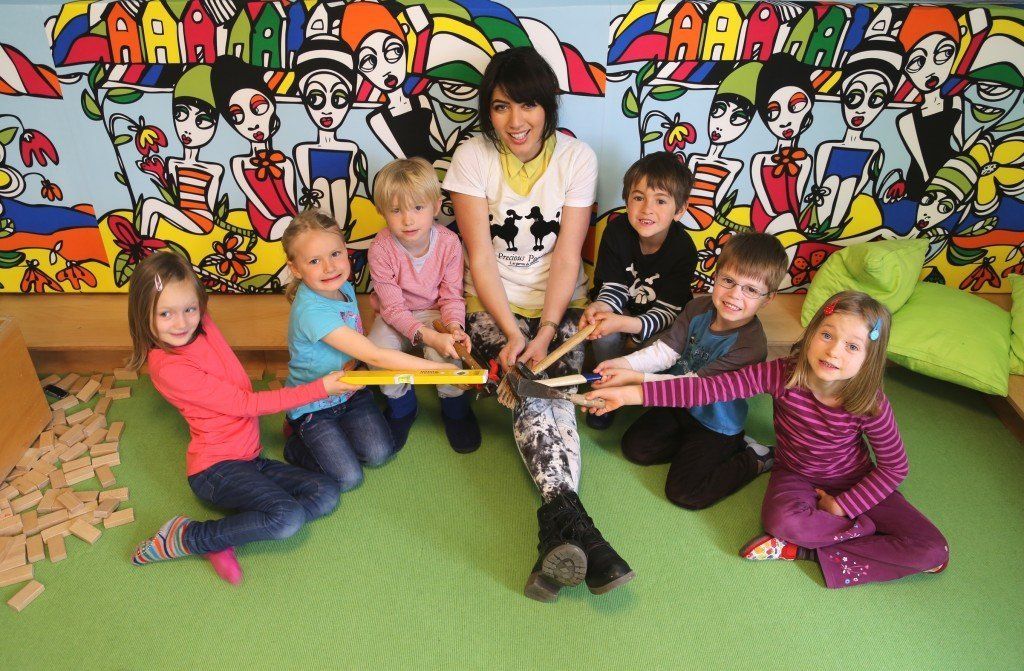 Eine Gruppe von Kindern sitzt um eine Frau herum, die ein Maßband hält