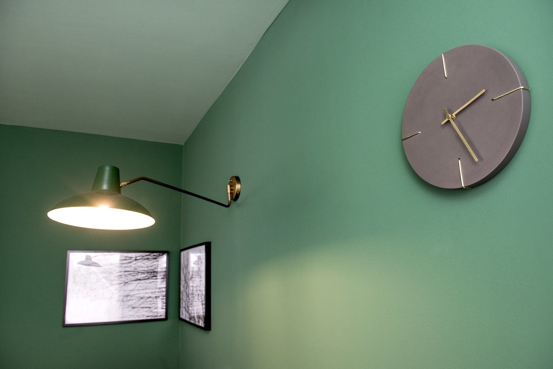 An einer grünen Wand hängt neben einer Lampe eine Uhr.