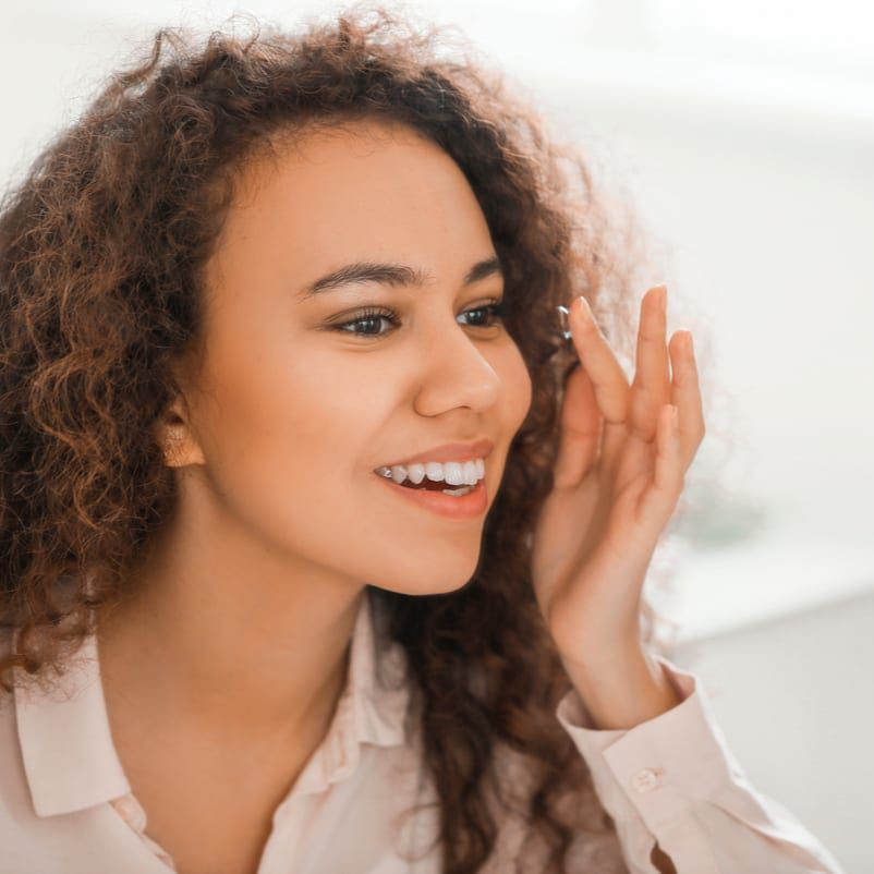 Smiling woman with a contact lens on the tip of her finger about to insert it into her eye