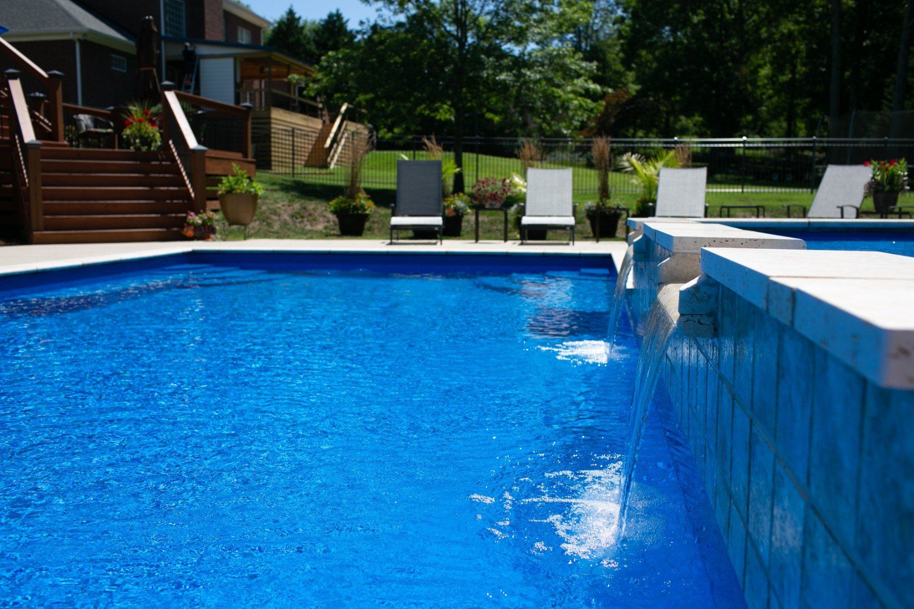 A large swimming pool with chairs around it and a house in the background