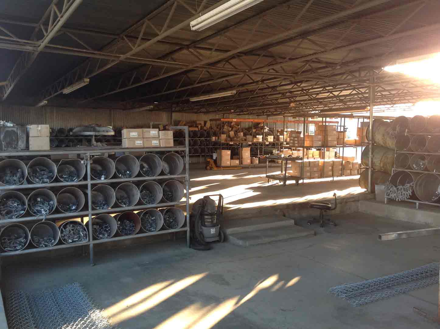 Warehouse interior with shelves of items, boxes, and coiled materials. Sunlight streams in.
