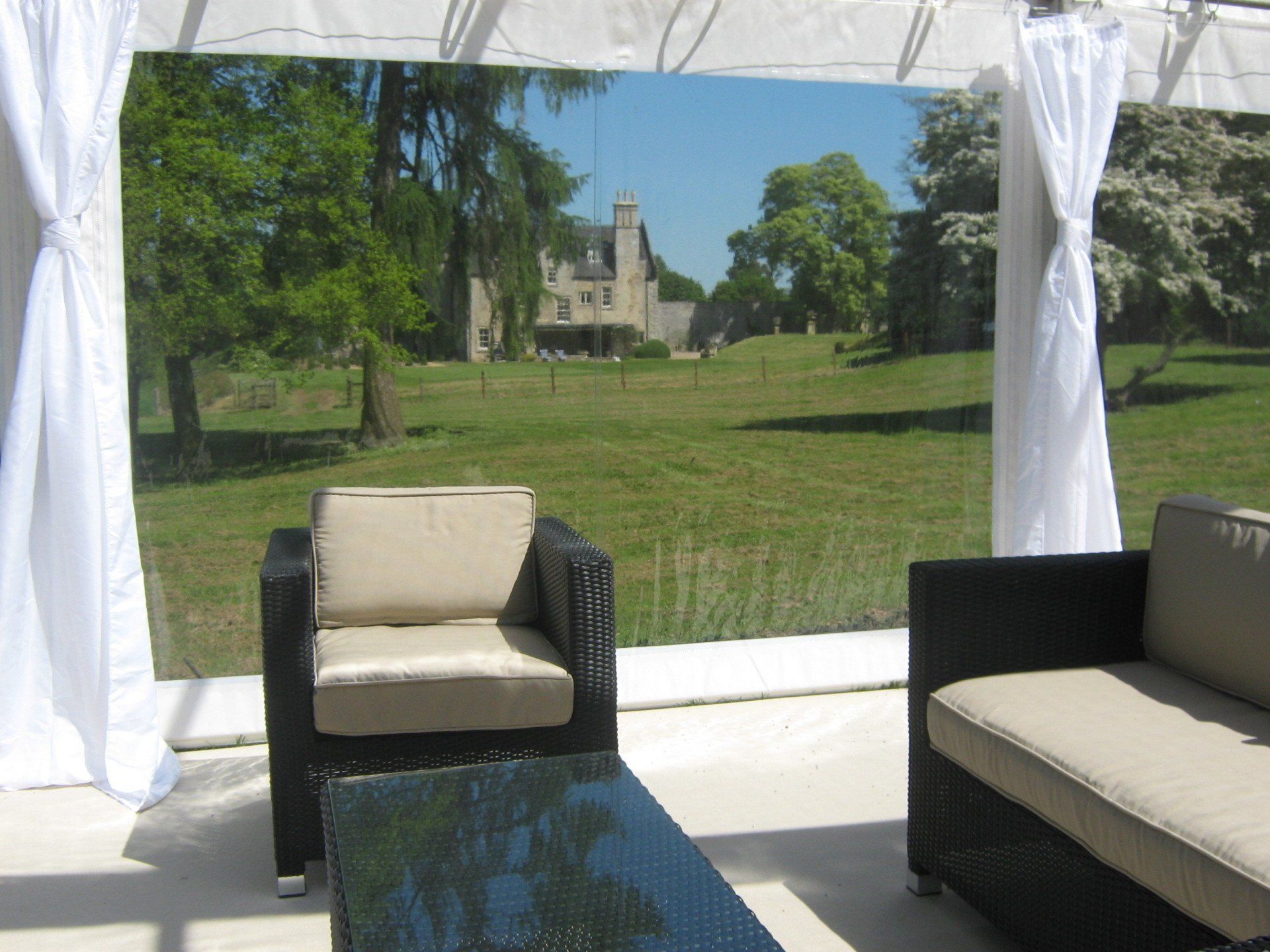 Outdoor lounge with a view of a castle. Black wicker furniture, white curtains, and green lawn.