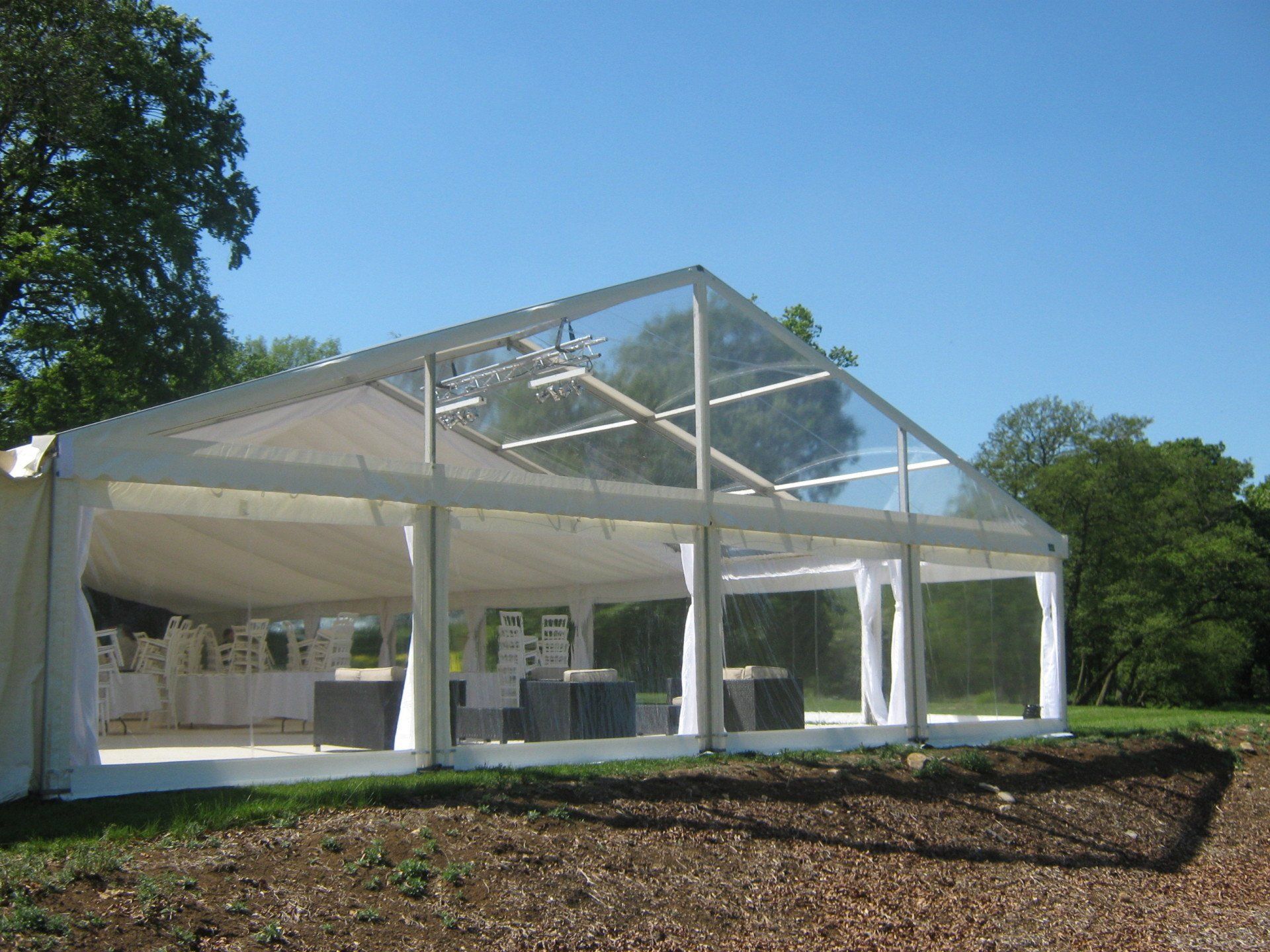 White and clear-roofed tent set up on green grass, with a clear blue sky background.