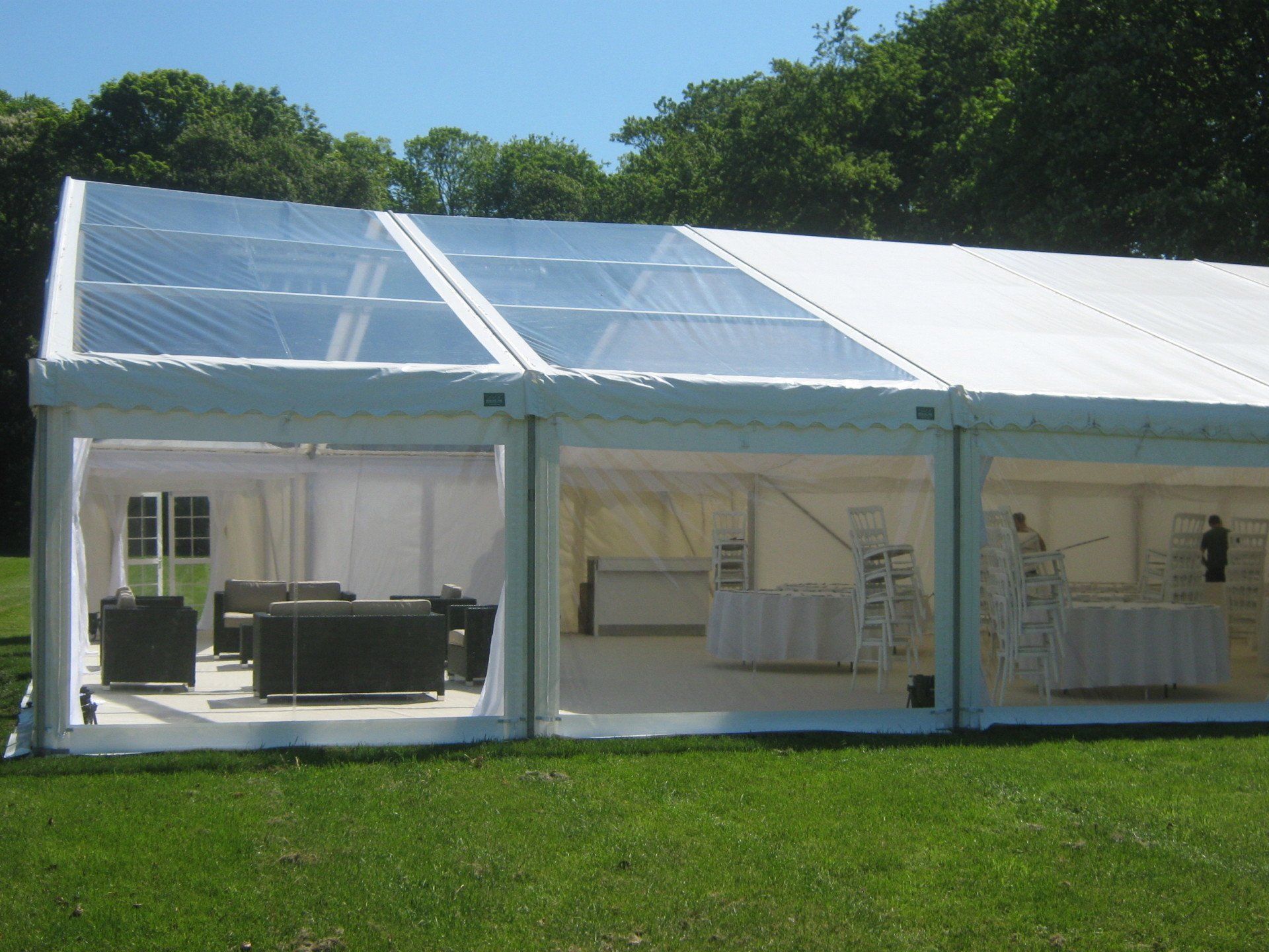 White party tent with transparent roof panels and clear side panels set on grass.