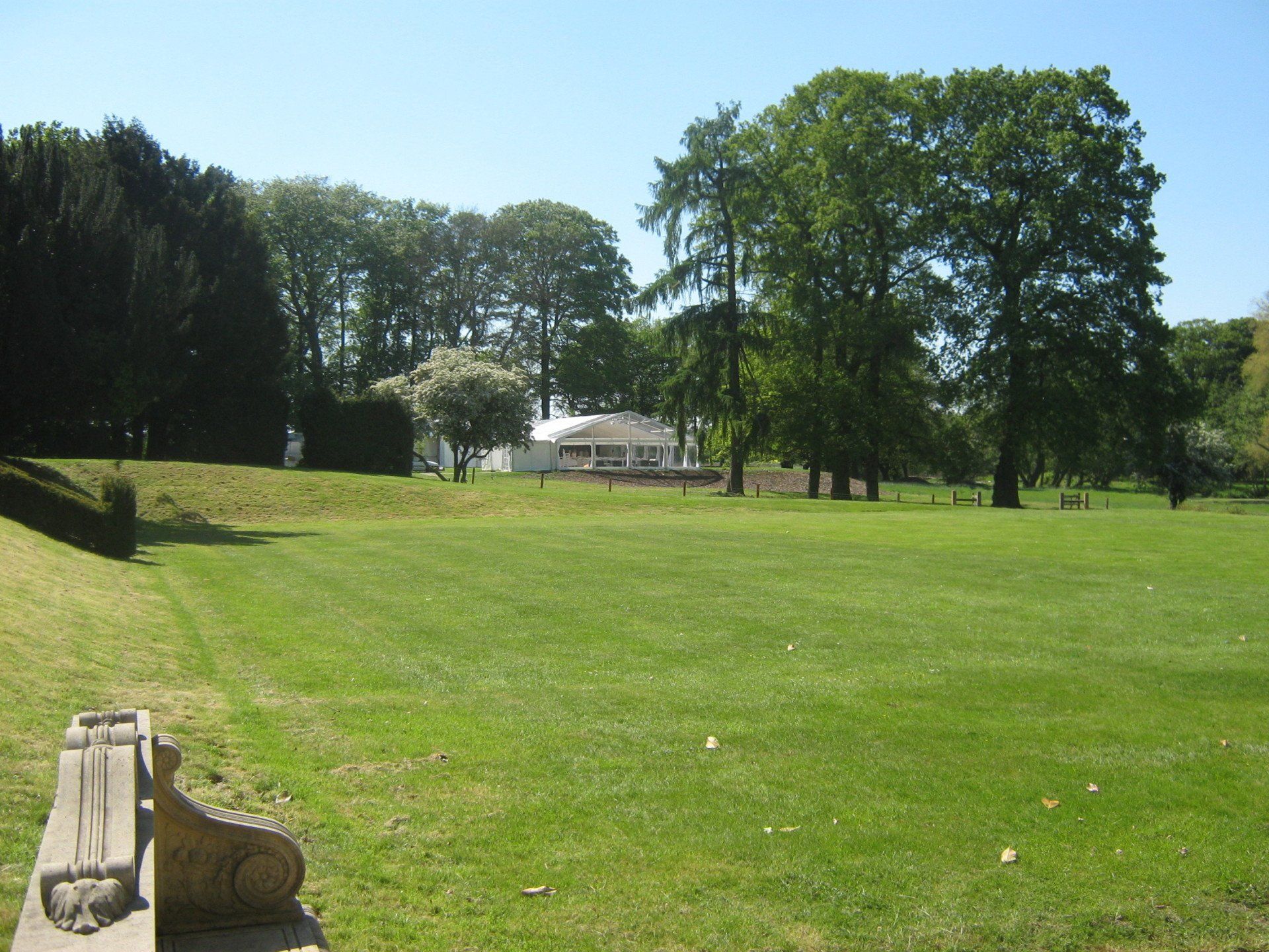 A grassy park with trees, a building in the distance, and a stone bench in the foreground.