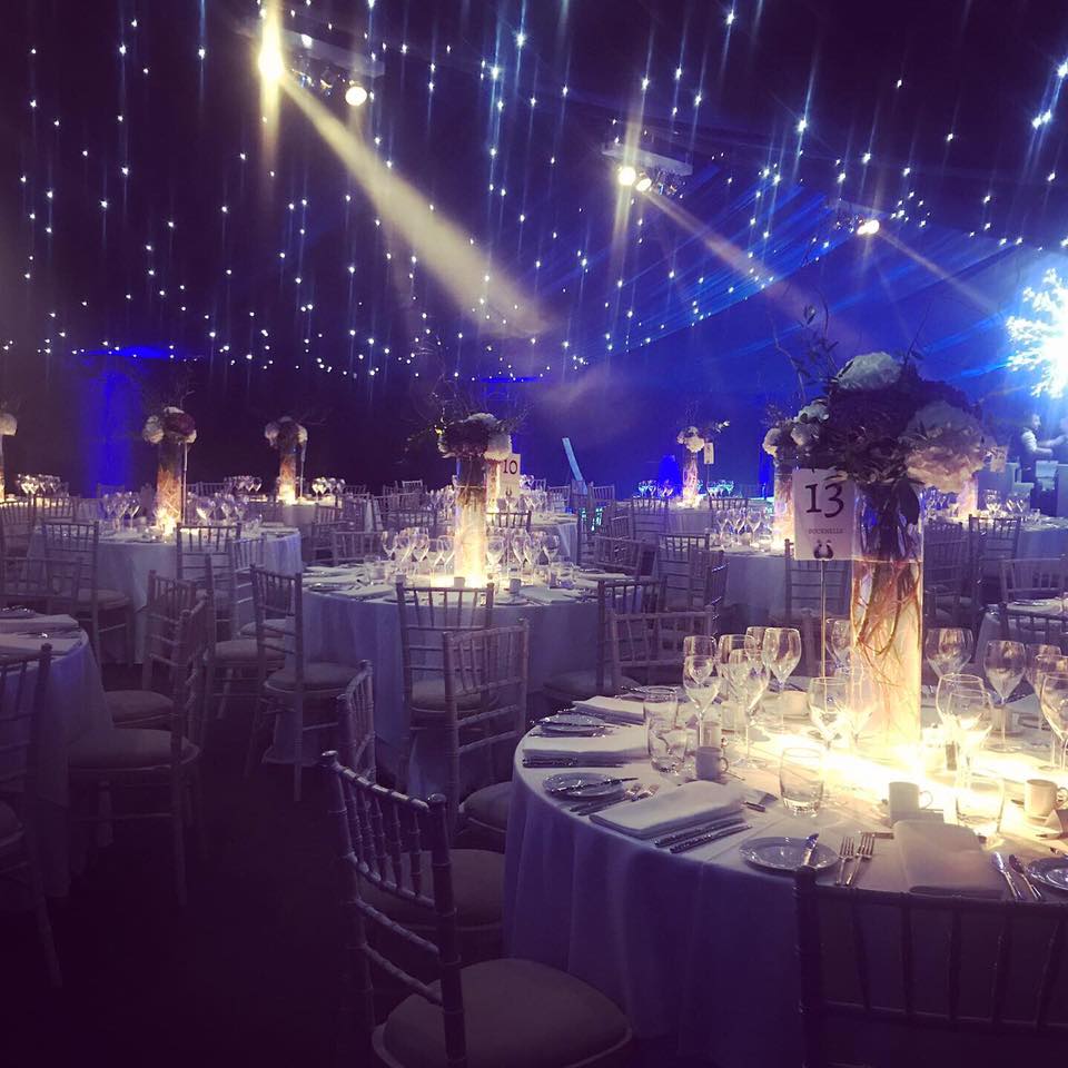 Elegant dining hall with white tablecloths, floral centerpieces, under starry ceiling. Table 13 visible.
