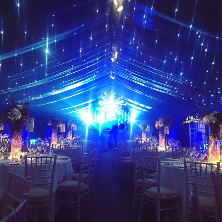 Elegant event tent with tables set for a party, blue and white lighting.
