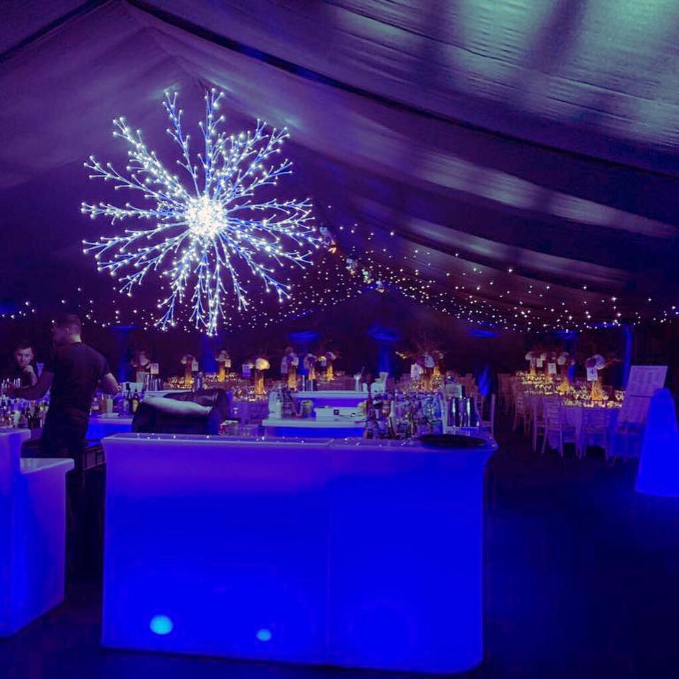 A dimly lit event space with blue glowing bar and snowflake light fixture, people seated at tables.