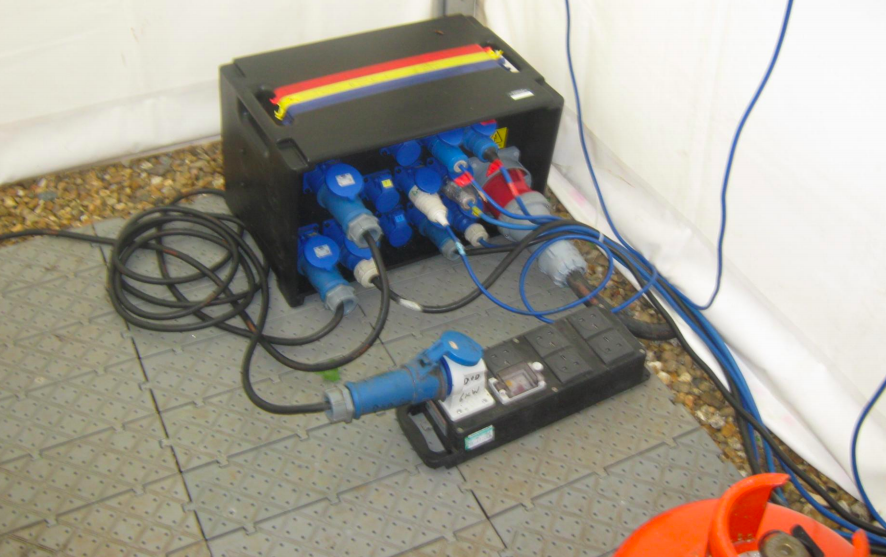 Black power distribution box with blue and red connectors, various cables, and a black ground box on a tiled floor.