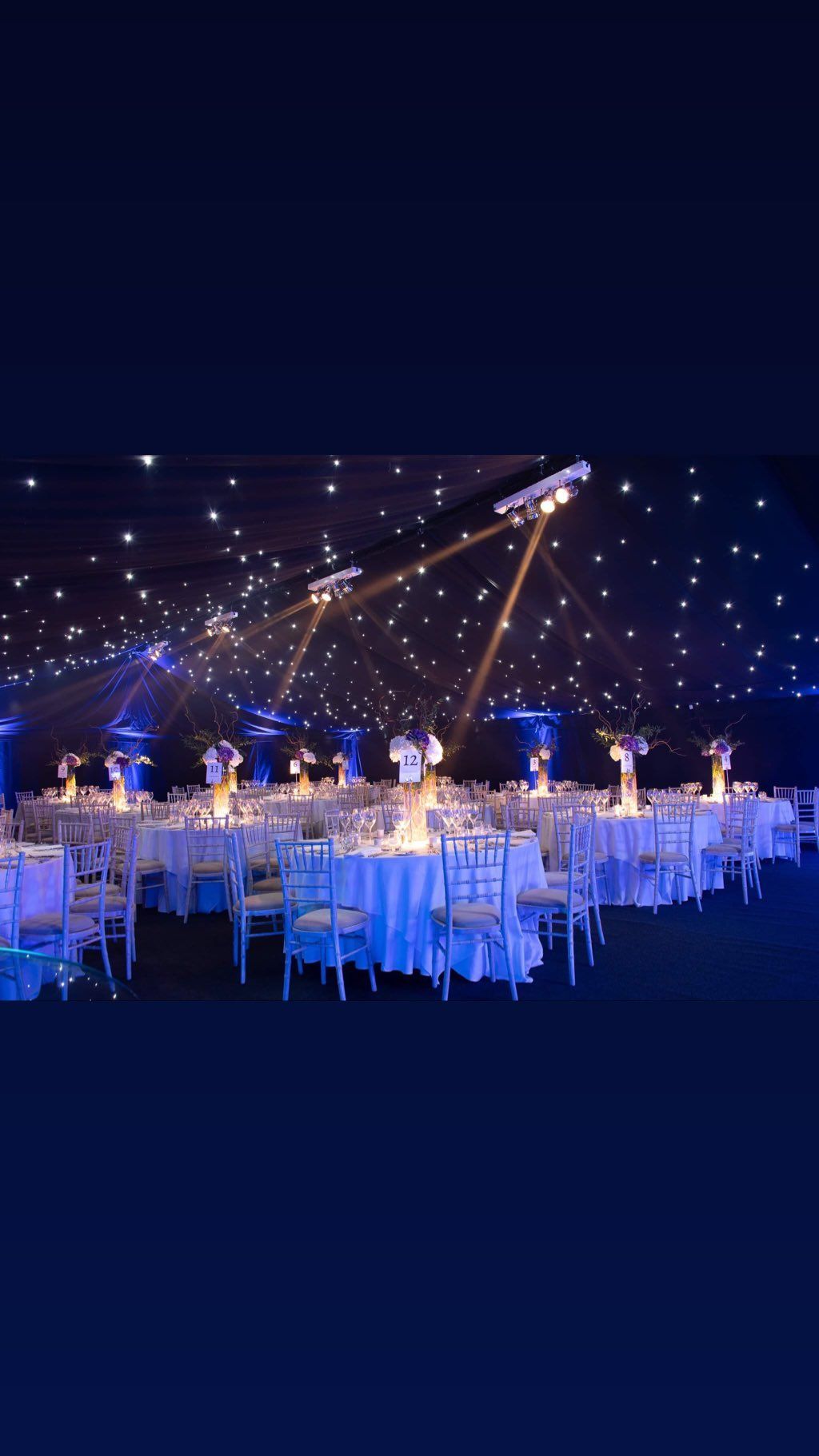 Elegant event space with tables, chairs, and starry ceiling, lit in blue and white.