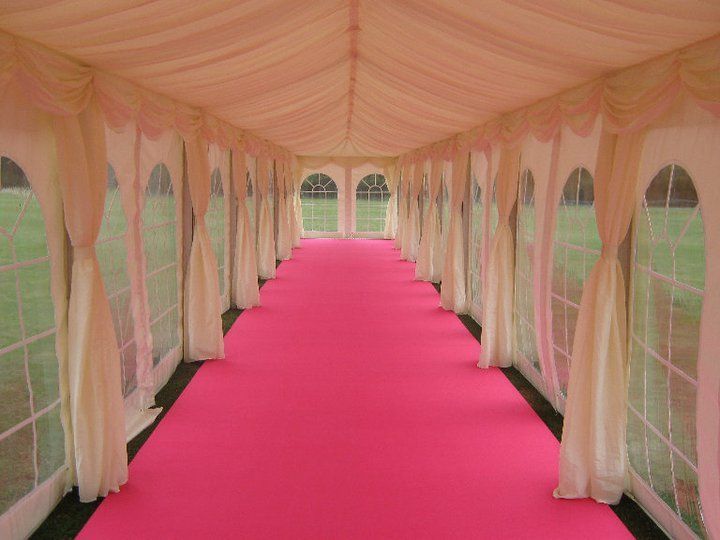 Interior of a white tent with a bright pink carpet runner; clear windows.