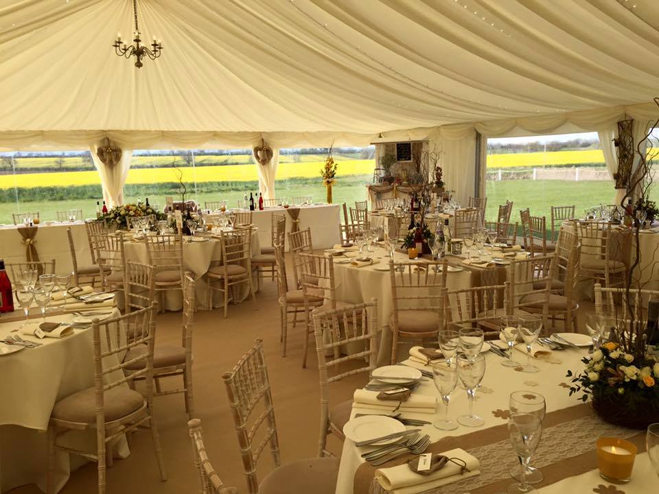 Wedding reception tent with tables, chairs, and floral centerpieces overlooking a field.