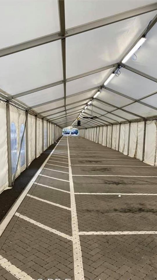 Long, empty drive-thru lane inside a large, white-roofed tent. White parking lines on the brick-like asphalt.