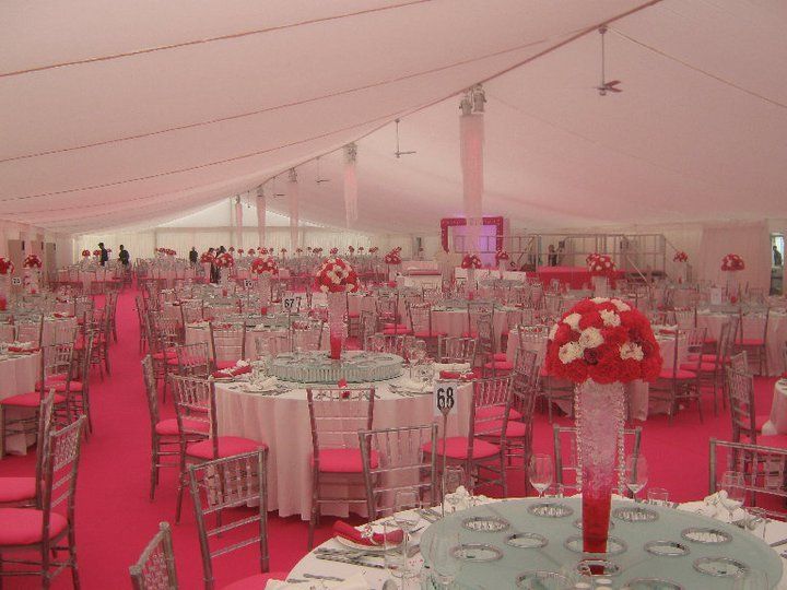 A large, pink tent interior set for an event with round tables, chairs, floral centerpieces, and a pink carpet.