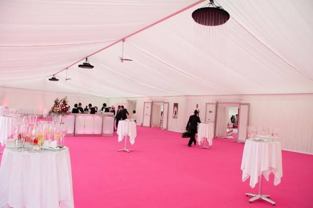 Interior of a large white tent with pink carpet and tables set for an event. Several people are visible.