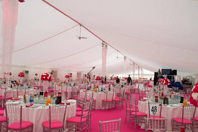 Pink and white decorated event tent with round tables, chairs, and centerpieces, filled with guests.