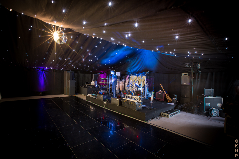 Inside a venue with black ceiling lights, a stage with musical instruments.