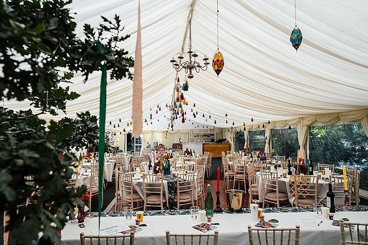 Wedding reception tent with tables, chairs, decorations, and hanging lights.