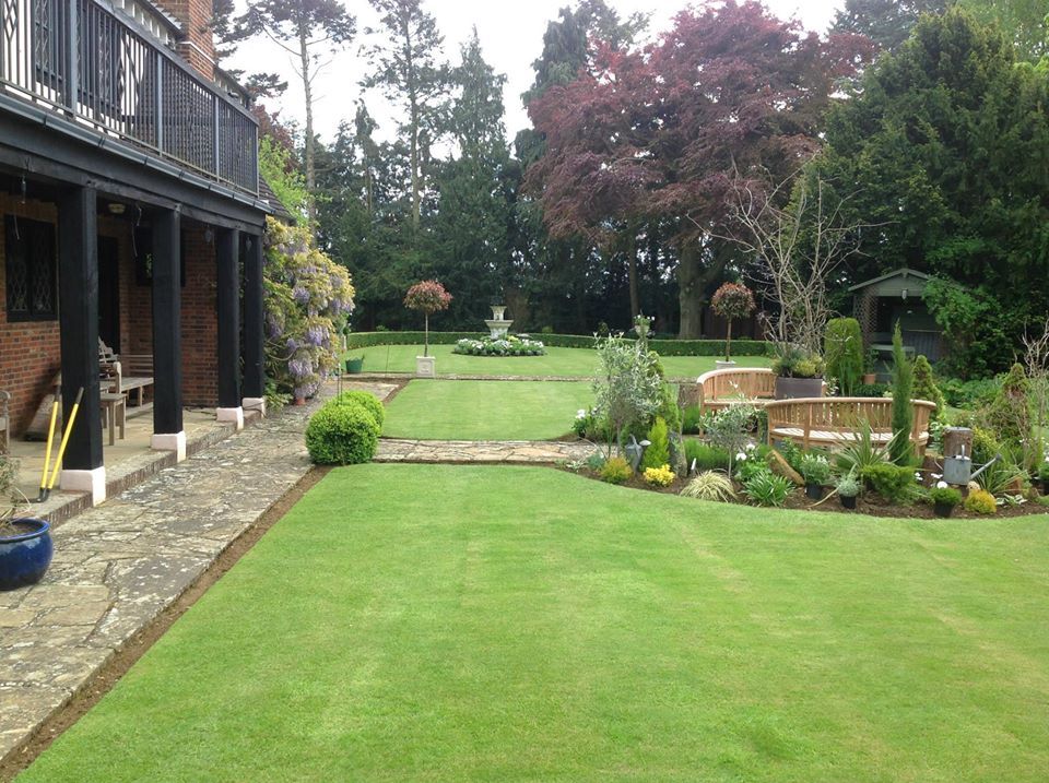 Well-manicured green garden with brick patio, landscaping and two-story house with black trim.