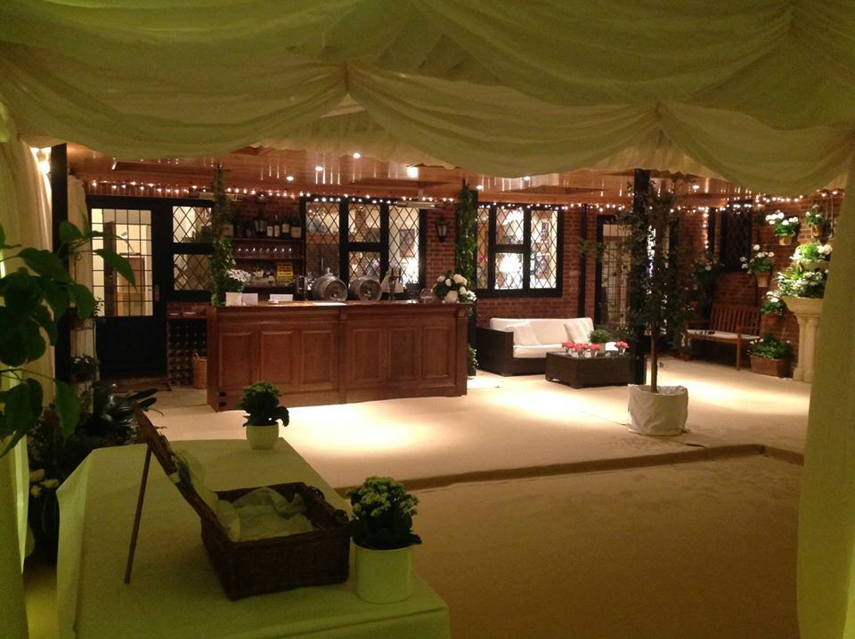 Elegant indoor event space with bar, seating, and draped ceiling. Soft lighting and decorative plants.