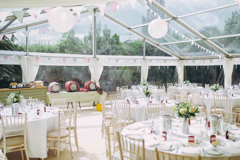 Wedding reception tent with round tables, white chairs, and decorations.