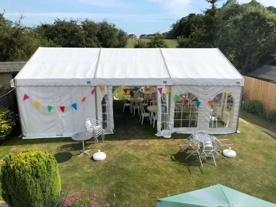 White party tent in a sunny backyard, decorated with bunting and containing tables and chairs.