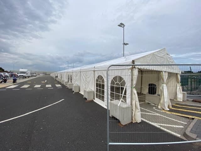 Long white tent structure with windows sits along a paved road, under a cloudy sky.