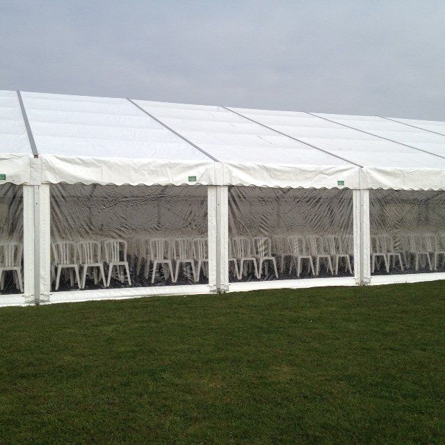 White tent set up on green grass, with rows of white chairs visible through transparent side panels.