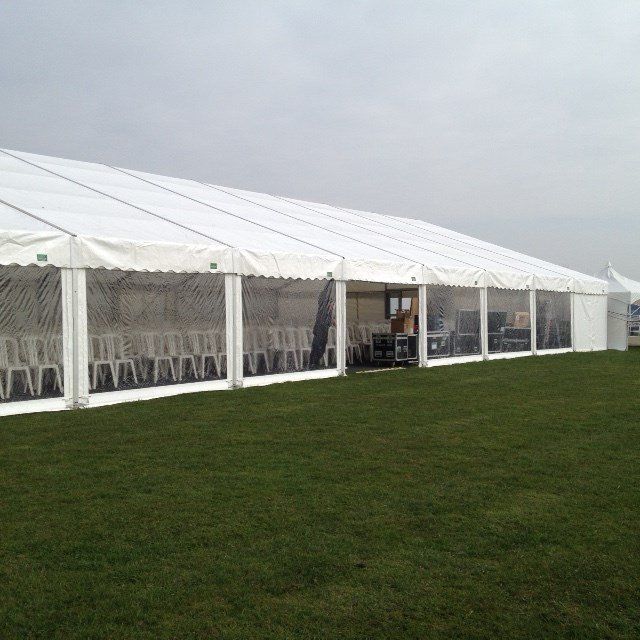 White tent with transparent side panels set up on a grassy field; rows of chairs visible inside.