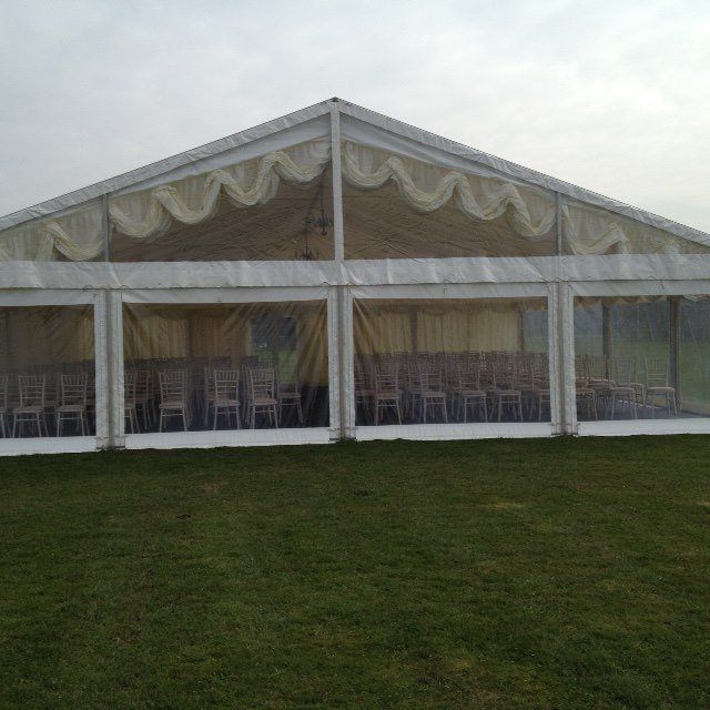 White tent set up on green grass, with chairs visible inside. Overcast sky in the background.