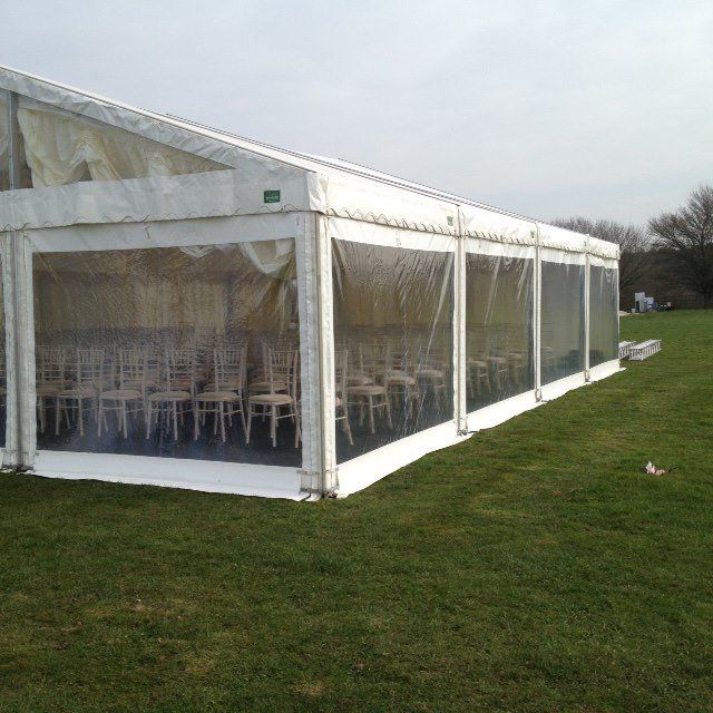 White tent with clear side panels on green grass; chairs inside.