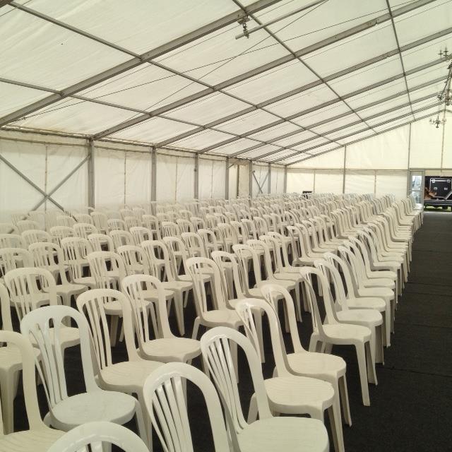 Rows of white plastic chairs in a large tent, set up for an event.