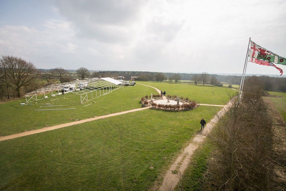 Overhead view of an open field with a white tent, a circular structure, and a flag blowing in the wind.