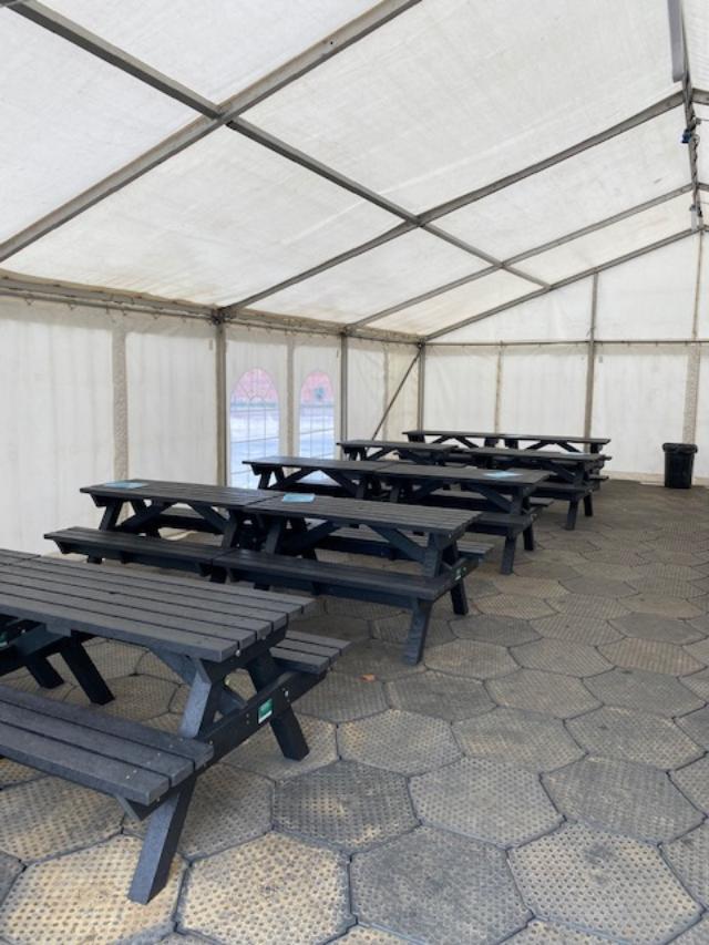 Picnic tables inside a white tent. Black tables and benches on a textured gray floor.