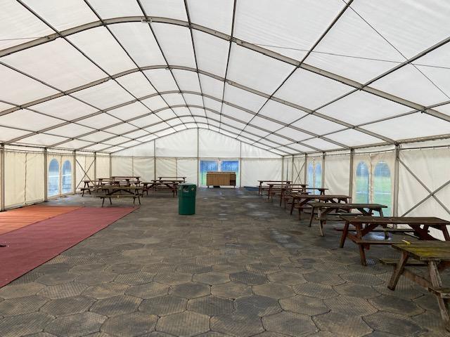 Large, empty tent with picnic tables inside. White roof and walls. Stone-like floor, red carpet on left.
