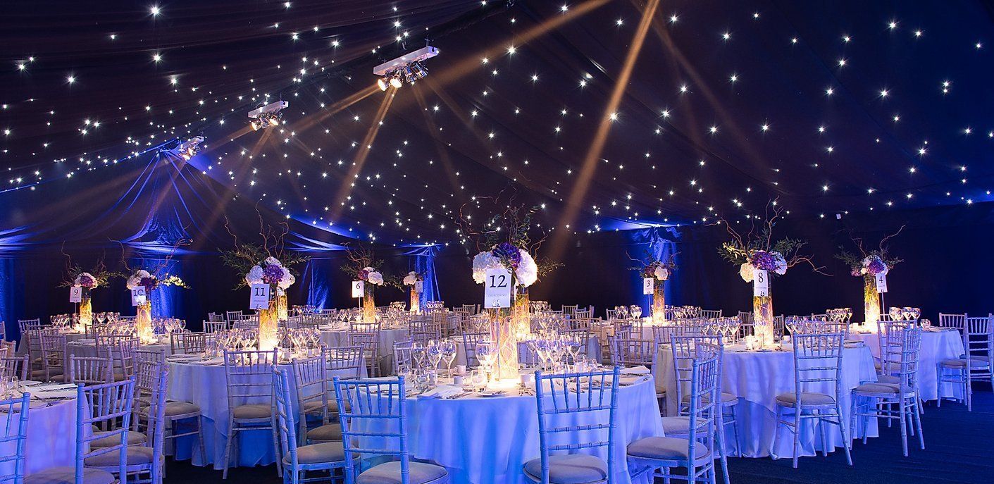 A beautifully decorated reception hall with starry lights and round tables set for a celebration.