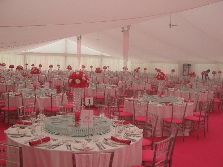 Large tent with round tables set for a formal event. Red and white decor, pink carpet.