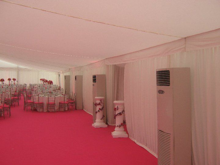 Inside a white tent: pink carpet, tables, chairs, decorative columns, and air conditioning units.