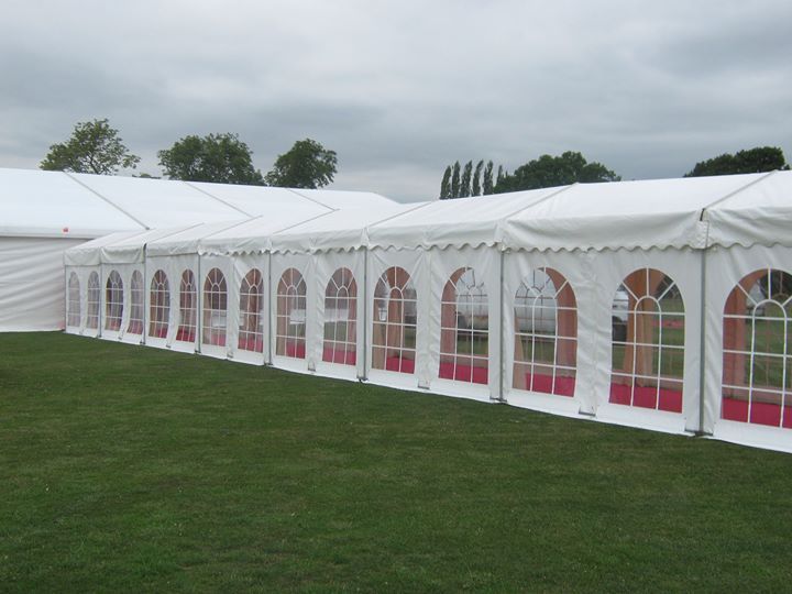 White tent with arched windows lined along green grass, under cloudy sky.