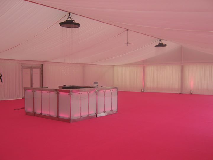 Interior of a white tent with a pink carpet, a lit bar, and lights hanging from the ceiling.